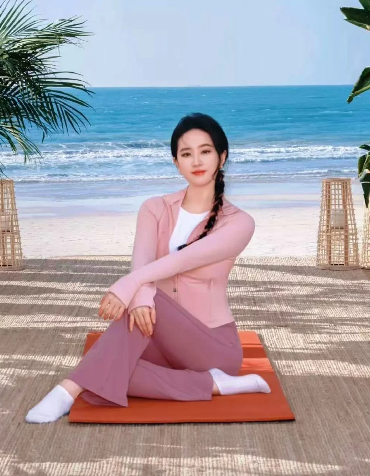 A woman by the sea, in a pink cardigan, sitting on a mat